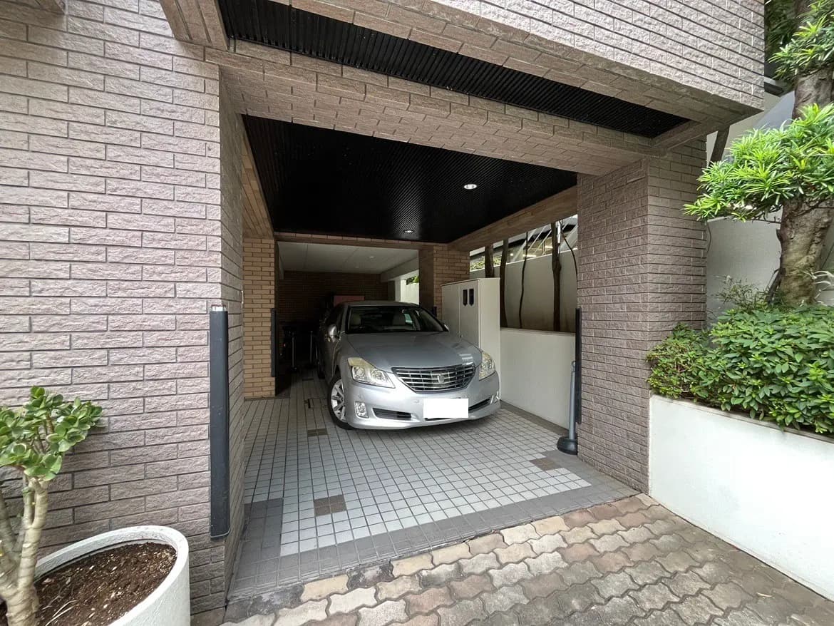 - ガレージに停められたシルバーのセダンと、モダンな外壁の住宅、周囲に緑があるエントランスの写真