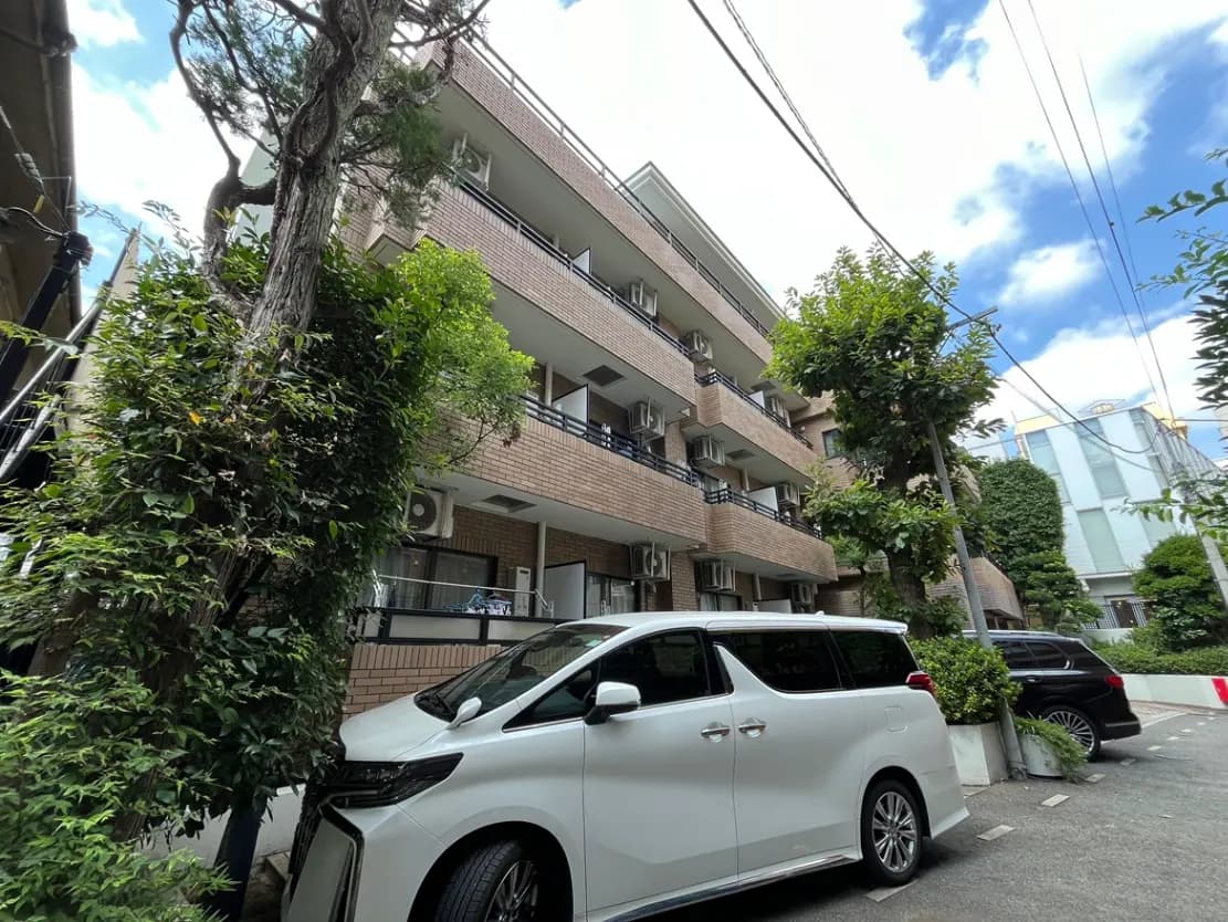 - 緑豊かな街並みに立つレンガ造りのマンション、白いミニバンが駐車している風景