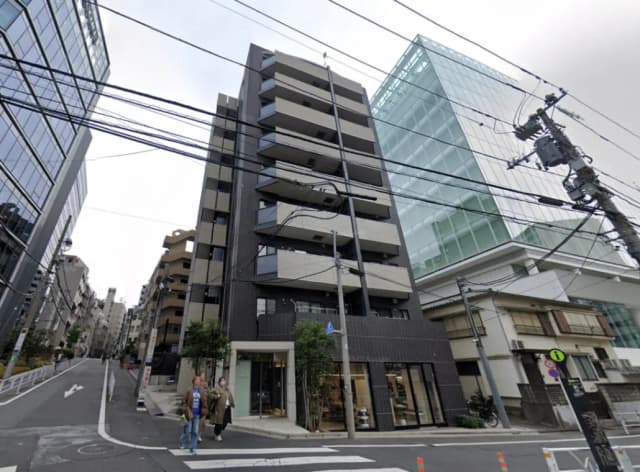 - モダンな外観の商業ビル、周囲には住宅やオフィスビルが立ち並び、歩道を歩く人々の姿が見える景観