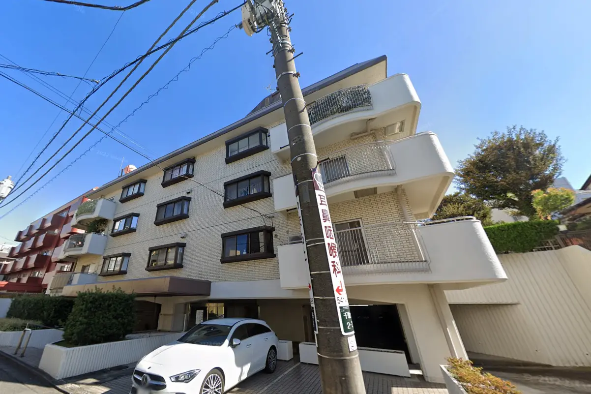 日本の都市部に位置する白い壁のマンション、屋根付きの駐車場とバルコニーが特徴的な外観デザイン