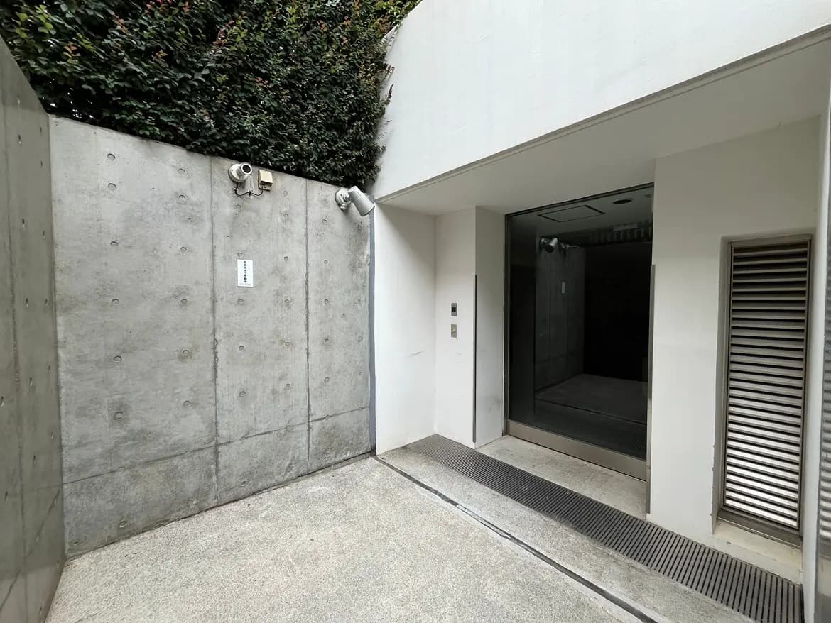 - コンクリートの壁と緑の植栽がある建物のエントランス、ガラス扉のアクセントが特徴的な外観