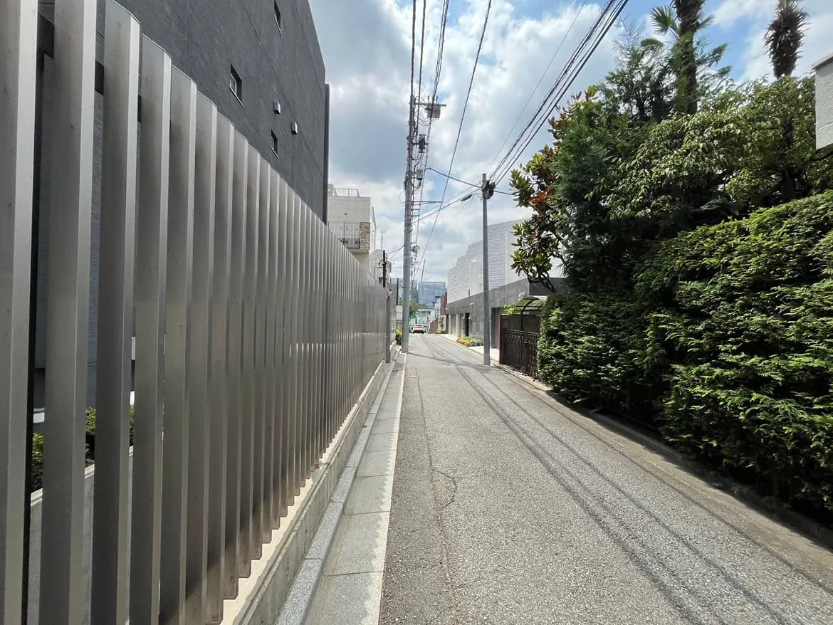 - 複数の建物に囲まれた静かな通り、金属製のフェンスと緑豊かな木々が並ぶ景観