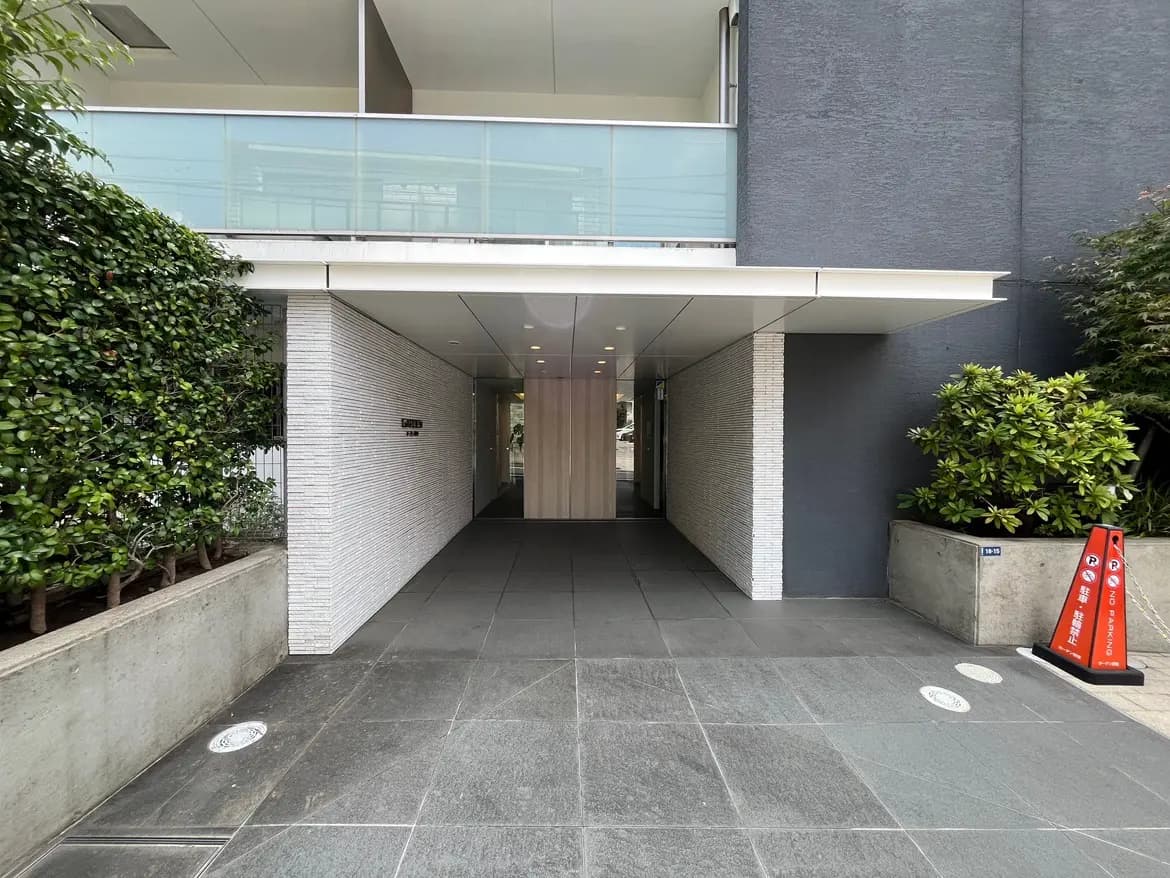 - モダンな建物のエントランス、滑らかな石材の床、緑の植物とシンプルな壁面デザインが特徴の入口