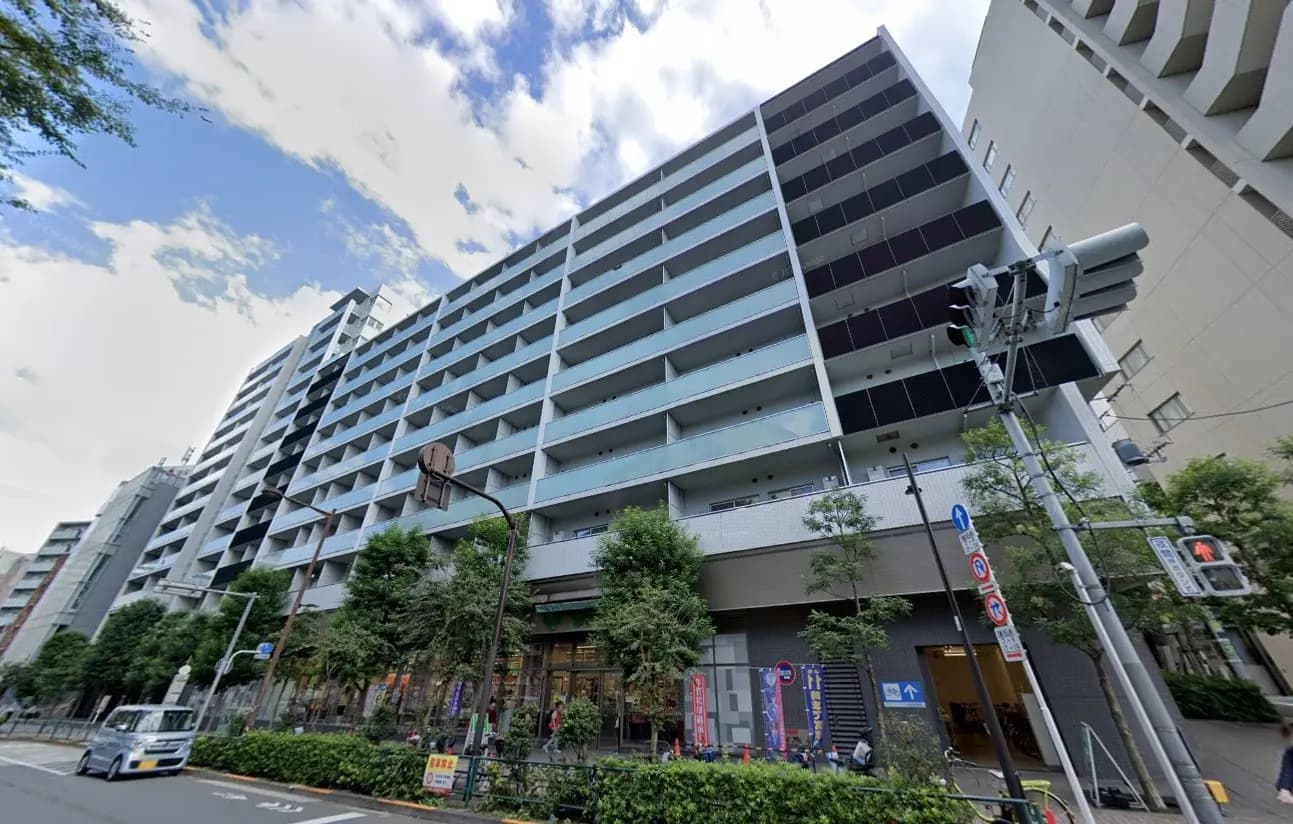現代的なデザインの都市型マンション、樹木が植えられた歩道、ショップが並ぶ一階部分