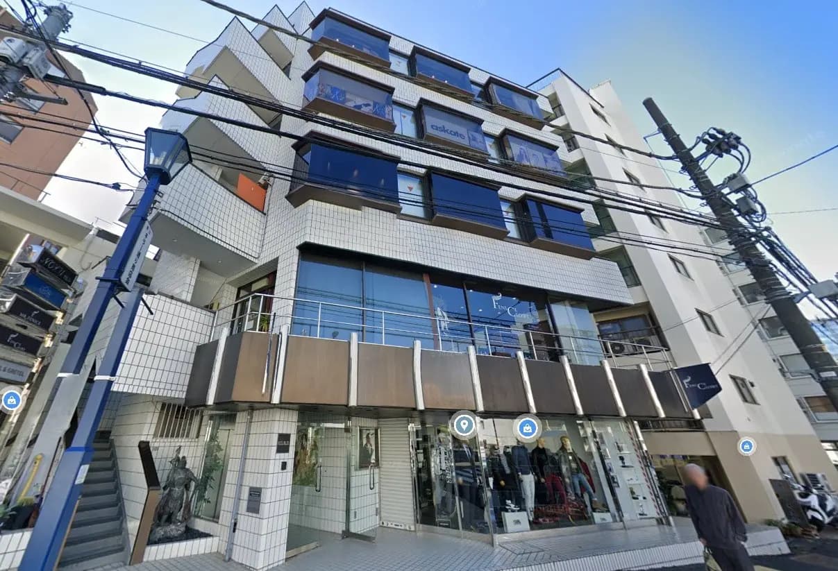白いタイル外観のモダンな商業ビル、路面店舗と住居が混在する建物、ブルーの看板とガラス窓