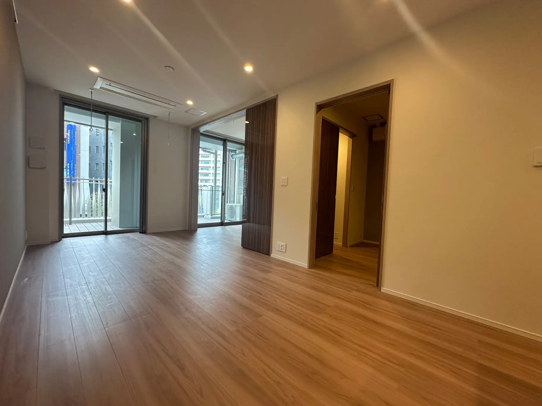 広々とした新築マンションのリビング、ナチュラルな木目調フローリング、バルコニー付きで明るい光が入る空間