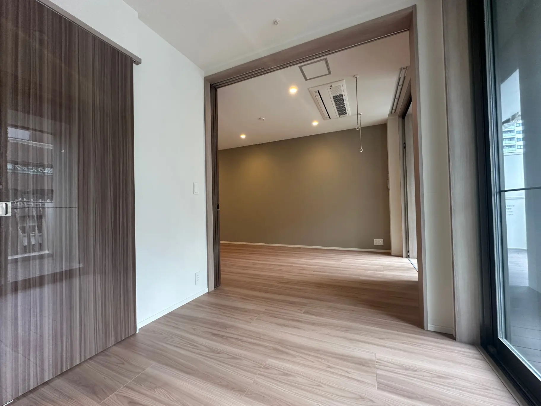 新築マンションの広々としたリビングルーム、木目調のフローリング、大きな窓からの自然光が魅力的な空間デザイン