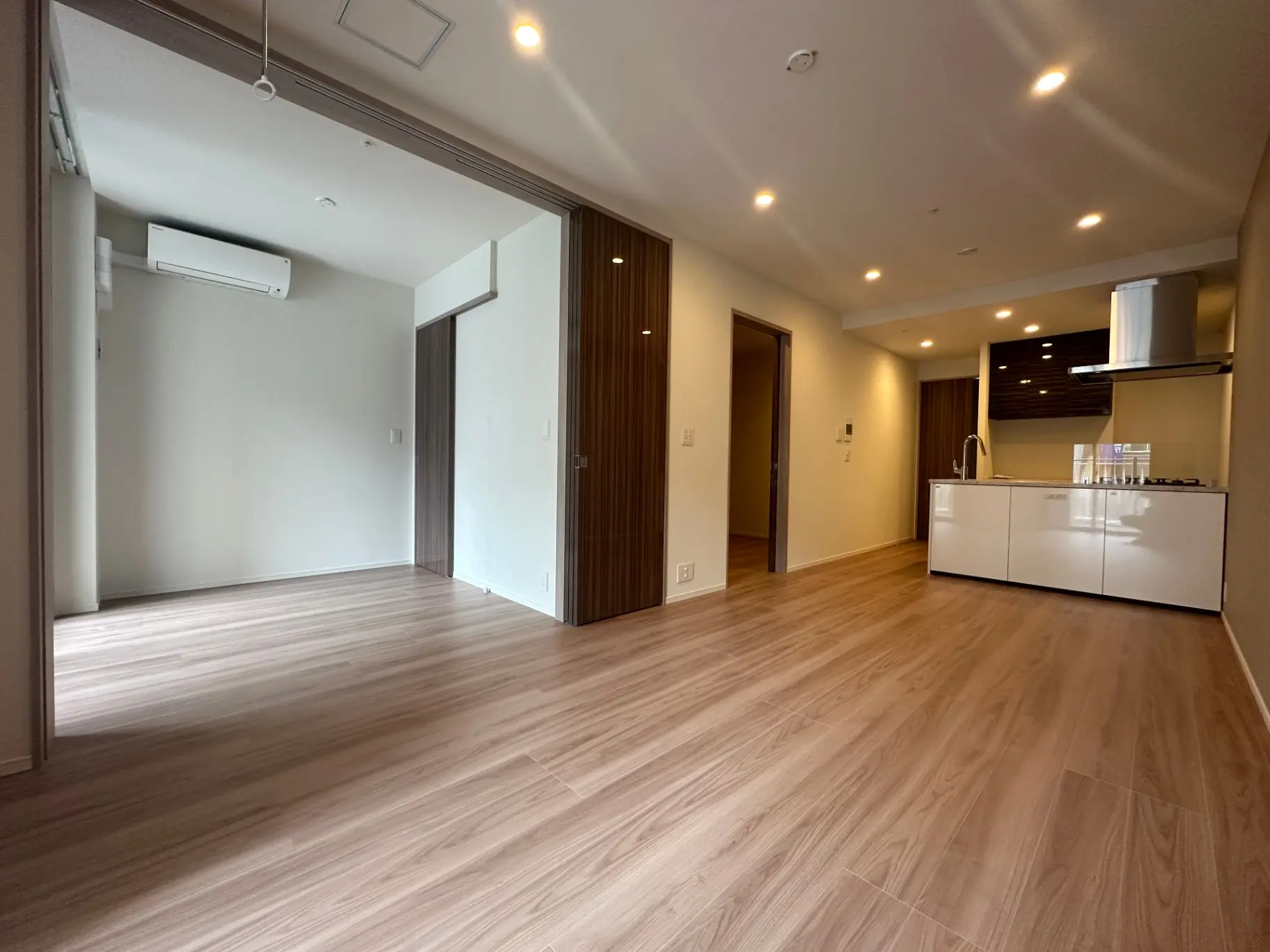 新築マンションの広々としたリビングダイニング、木目調フローリング、明るいLED照明付き天井