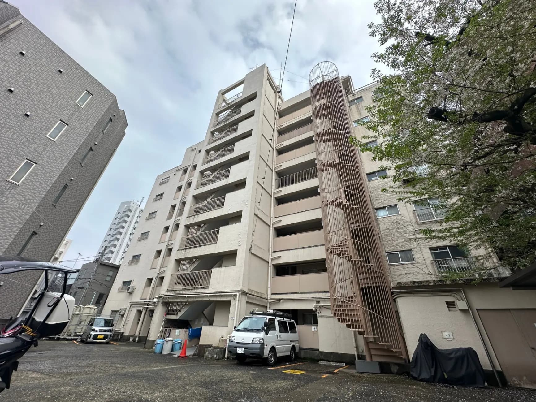 都市の風景、マンションの中庭、駐車場と桜の木、曇り空