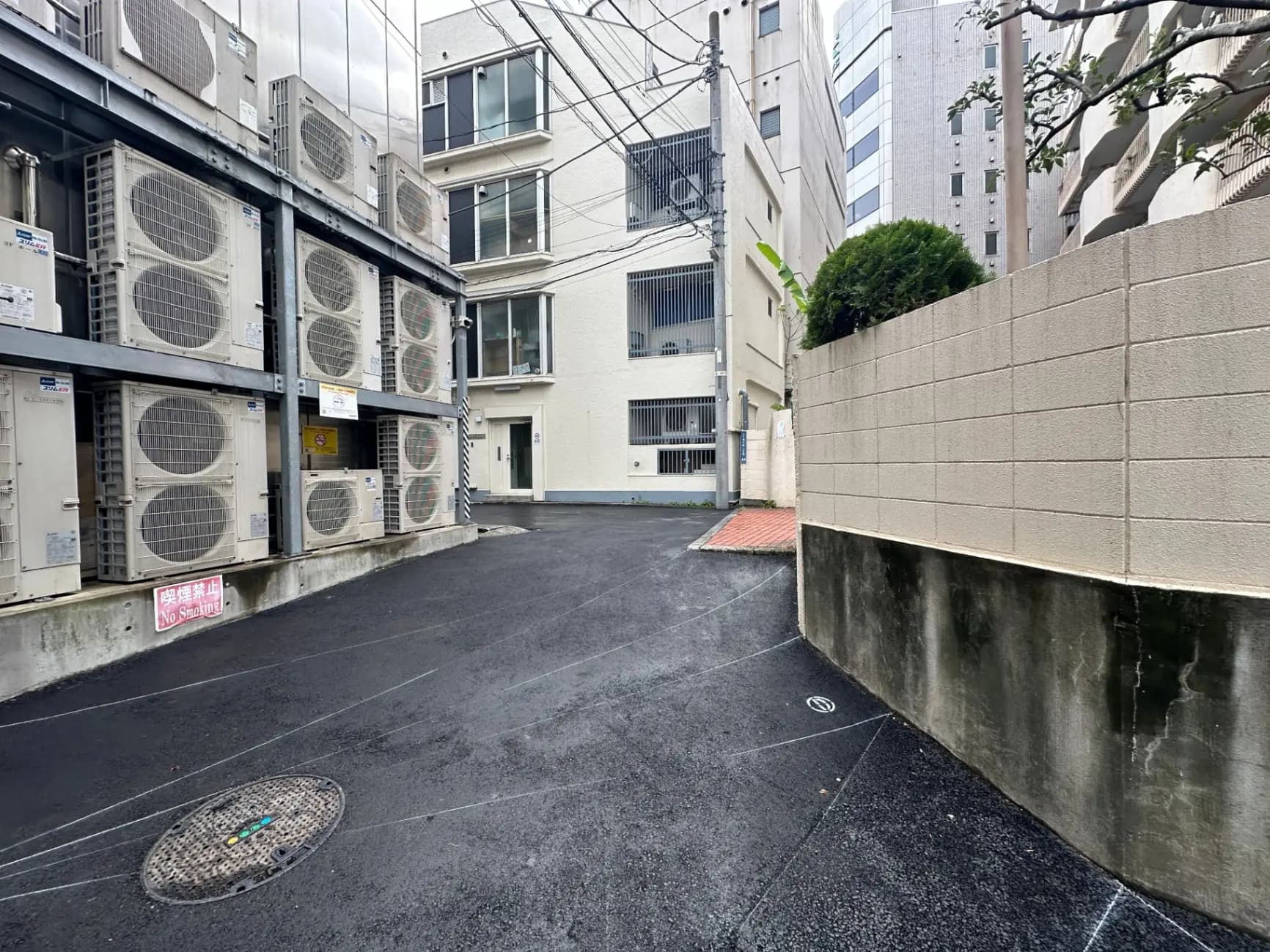都会の裏路地に並ぶ多数のエアコン室外機、禁止駐車の看板、コンクリートの壁