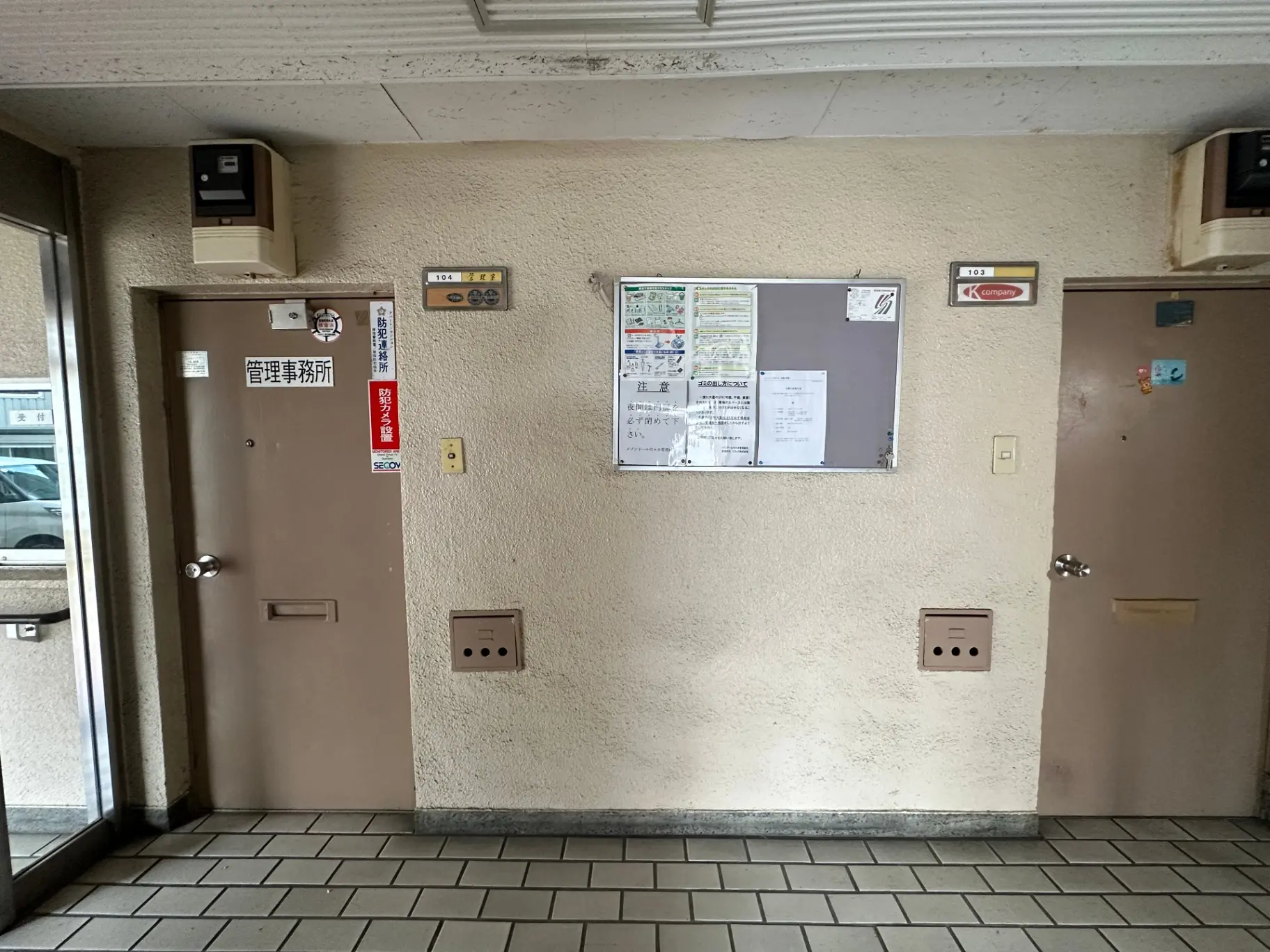 日本のマンションのエントランス、掲示板と郵便受けが設置された壁、玄関ドアとインターホン