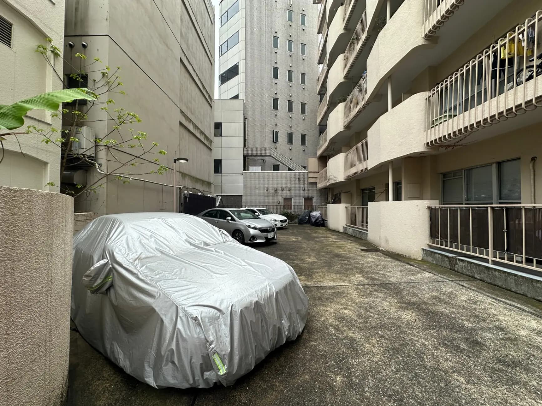 都市部の駐車場に保護カバーをかけられた車とアパートメントビルの光景