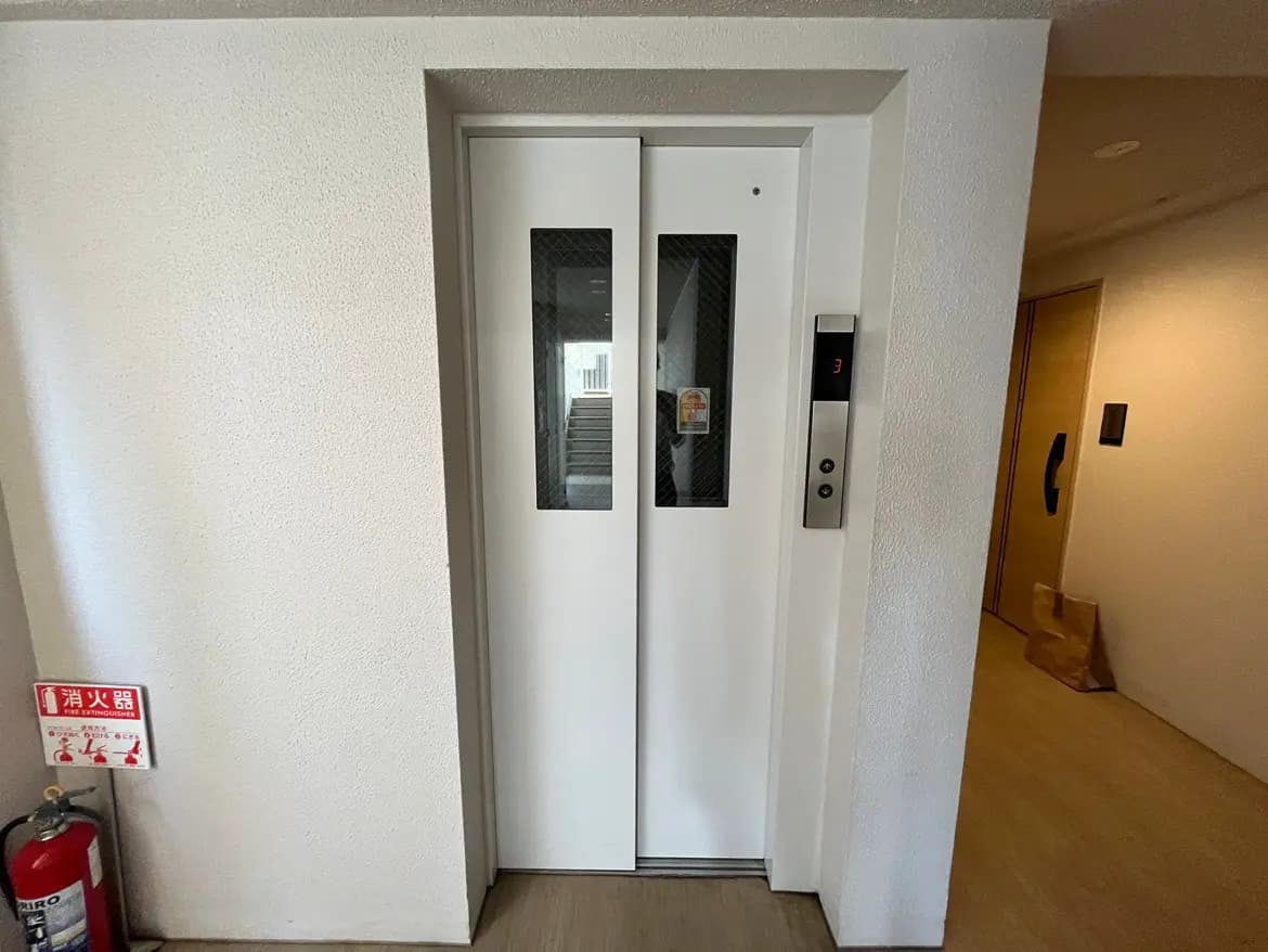 - モダンなデザインのエレベーターの入り口、白い扉と透明な窓、近くに消火器が設置された建物の内部