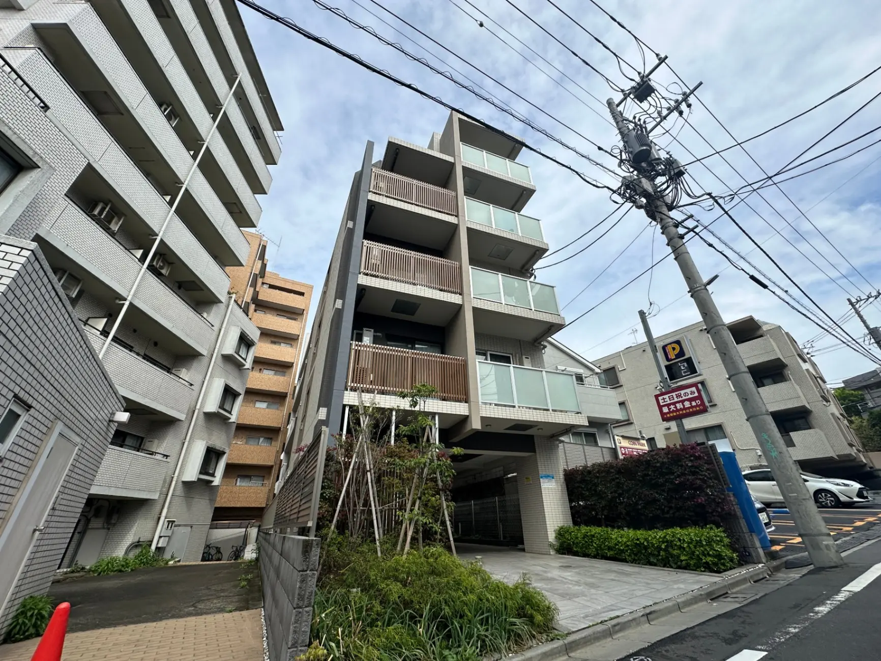 日本の都市部にあるモダンなマンションの外観、駐車場付き、電柱と配線が目立つ通り沿い