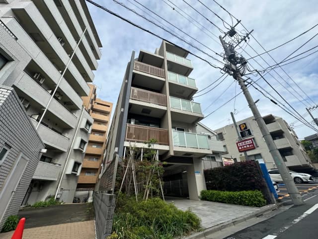 日本の都市部にあるモダンなマンションの外観、駐車場付き、電柱と配線が目立つ通り沿い