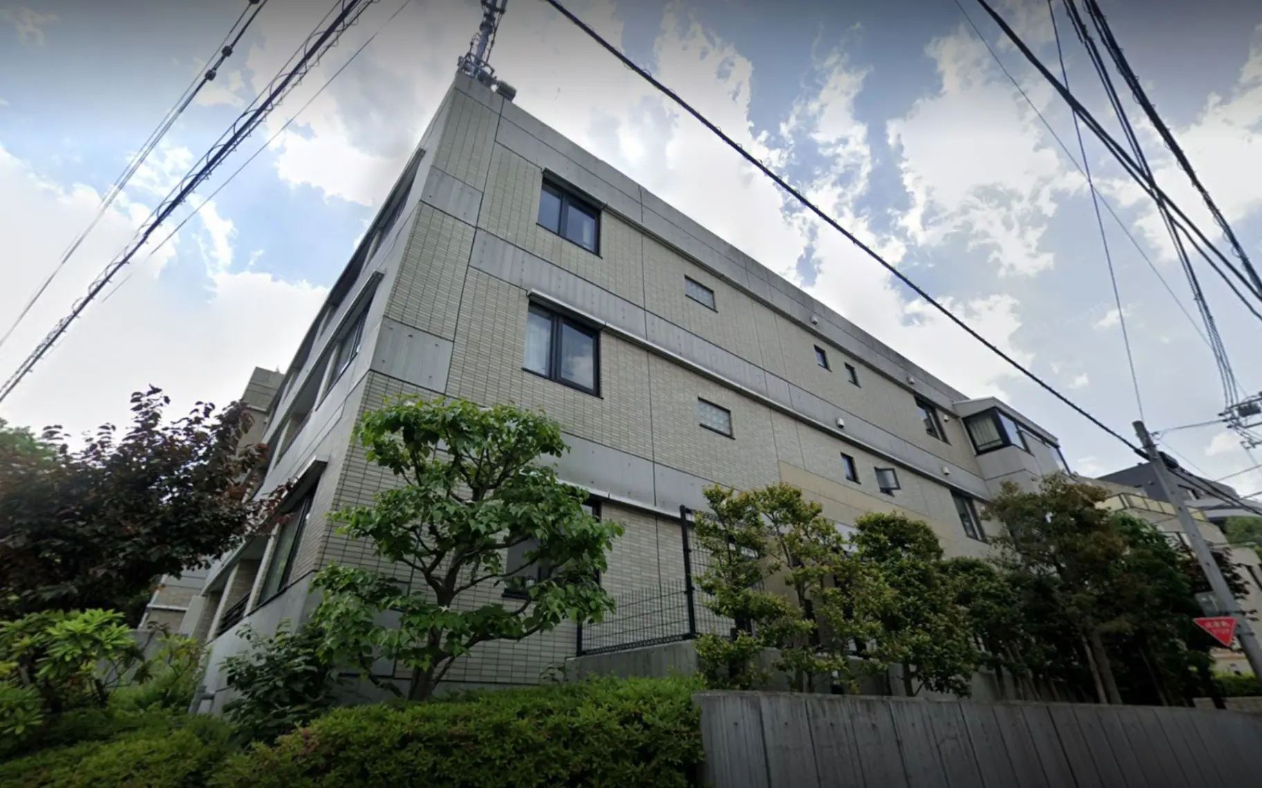 都会の住宅街に立つ現代的な外観のマンション、周囲に緑豊かな植栽
