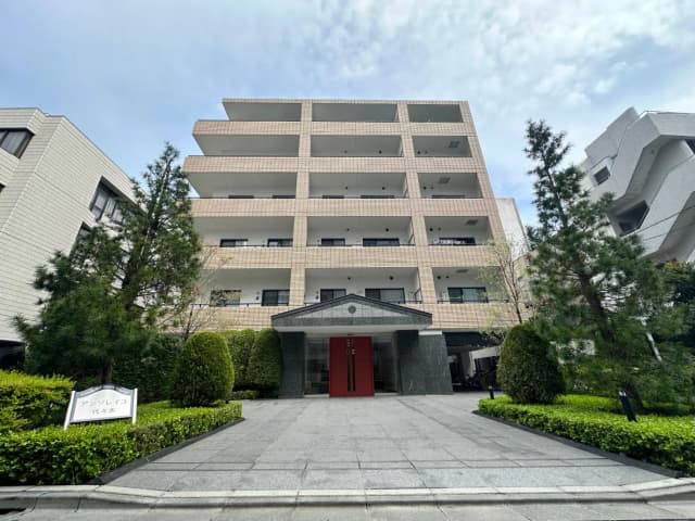 高級感あふれるマンションのエントランス、緑豊かな庭園、赤いドアがアクセント