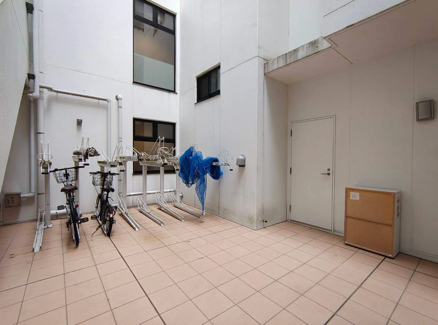 - 自転車二台が置かれた屋外スペース、白い壁と大きな窓が特徴のクリーンな雰囲気、荷物置き場と洗濯物干しがあるエリア
