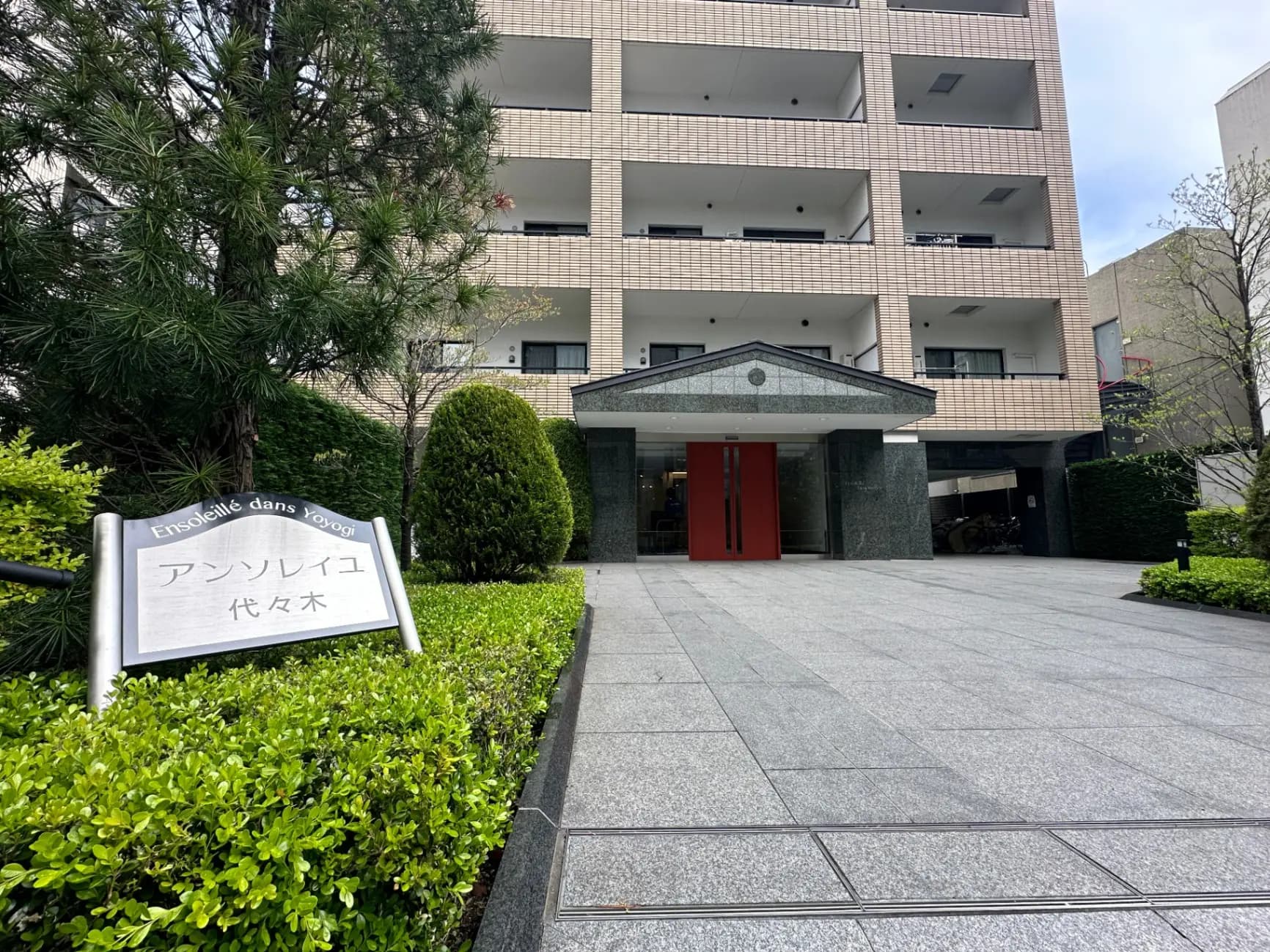 アンソレイユ代々木と書かれた看板のあるモダンなマンションのエントランスと緑豊かな庭