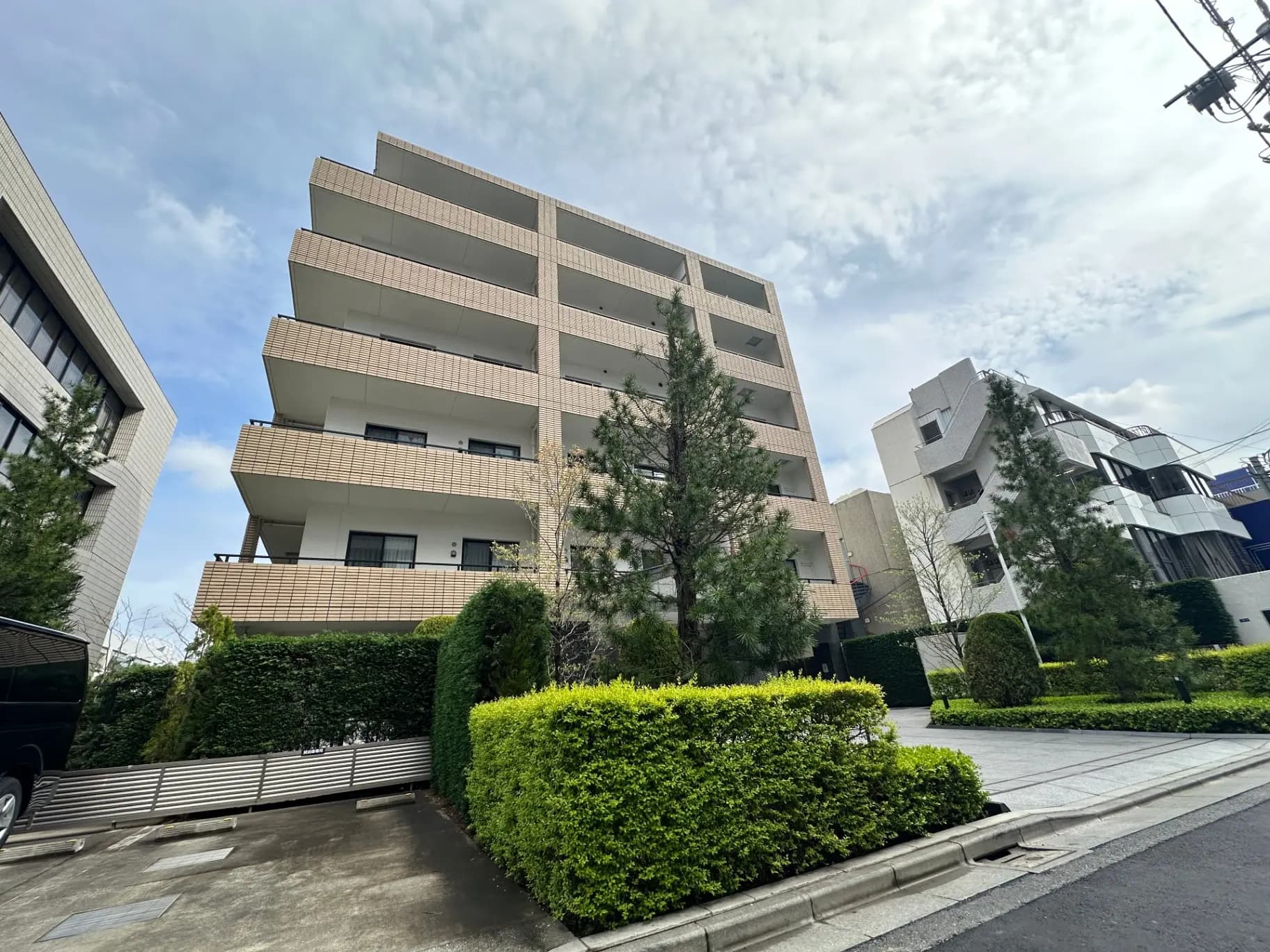 モダンな外観の都市型マンション、緑豊かな植え込みと整備された駐車場