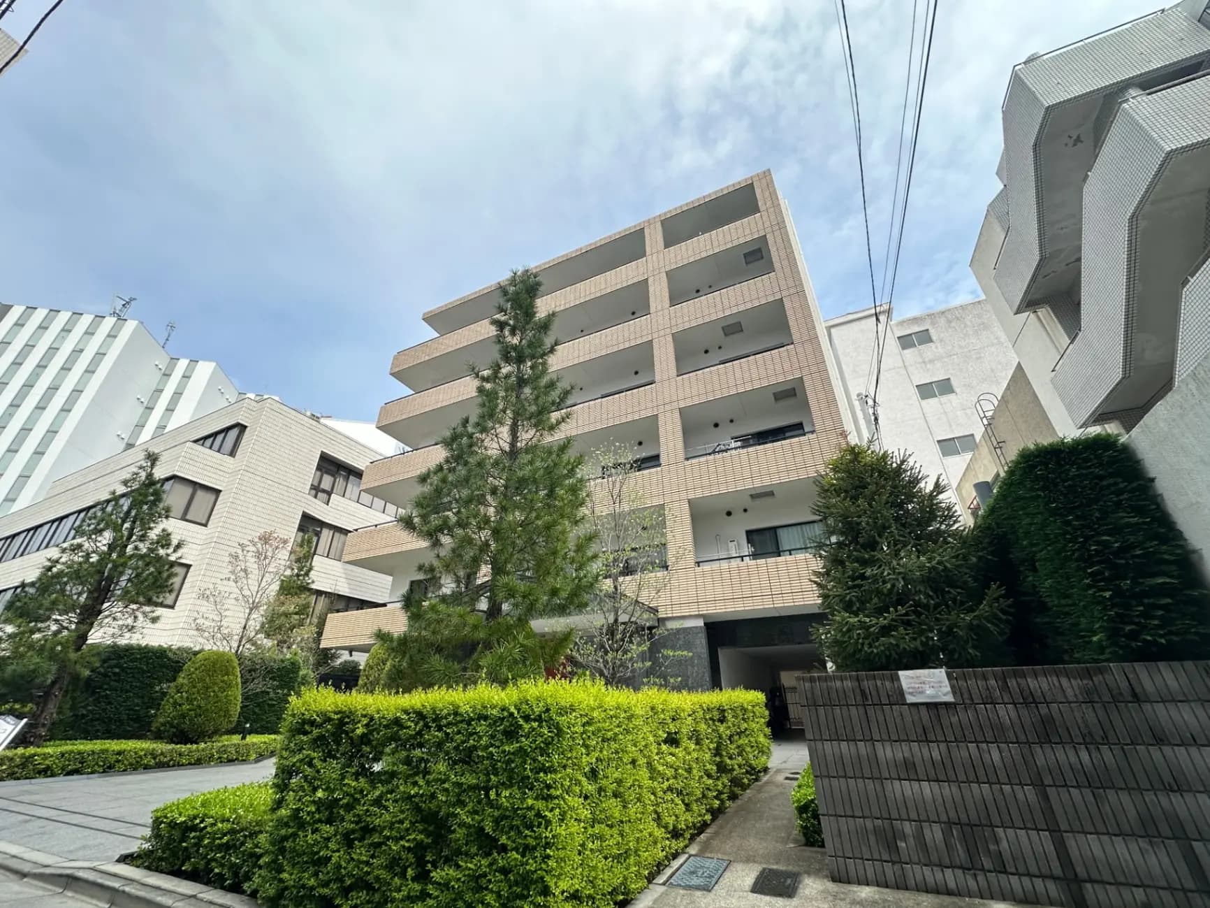 都市の景観を映す現代的なマンション、緑豊かな庭園と街路樹、晴れた日の青空