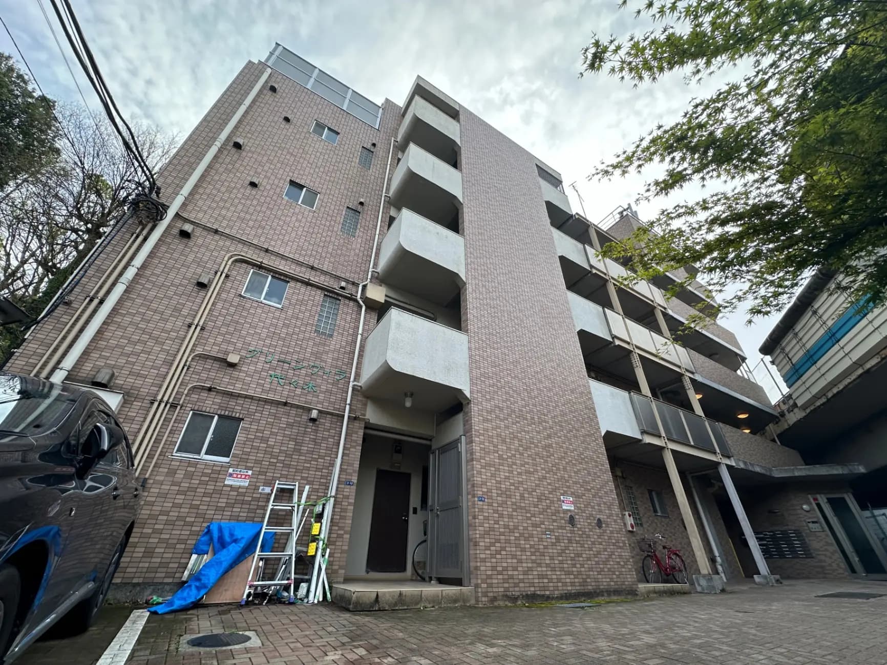 日本の住宅街にある多階建てのアパートメントビル、茶色いタイル張りの外壁とバルコニー、青空と緑の木々が見える景色