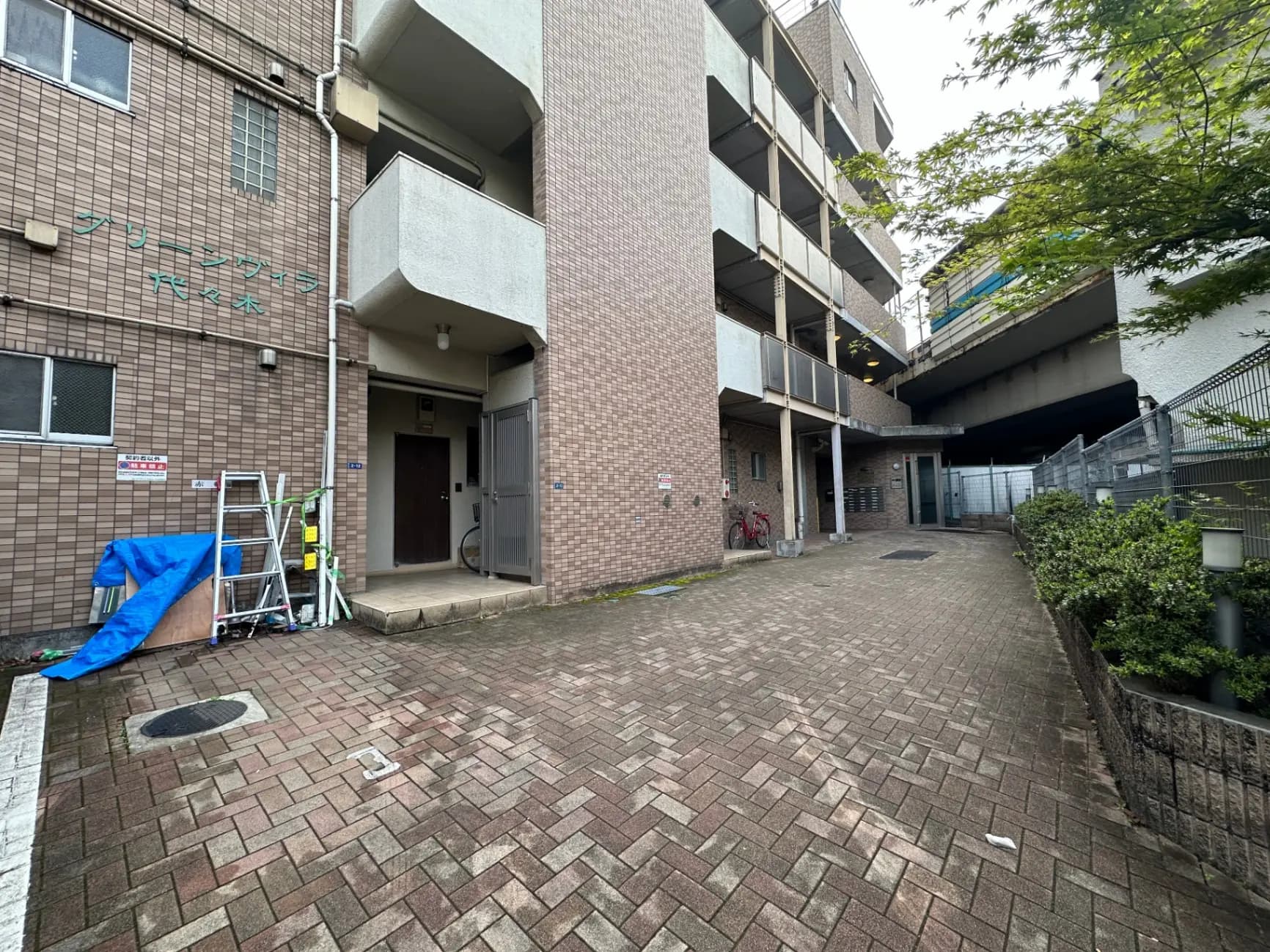 日本の都市のマンション外観、茶色のタイル張り、入り口と自転車置き場が見えるアパートメント
