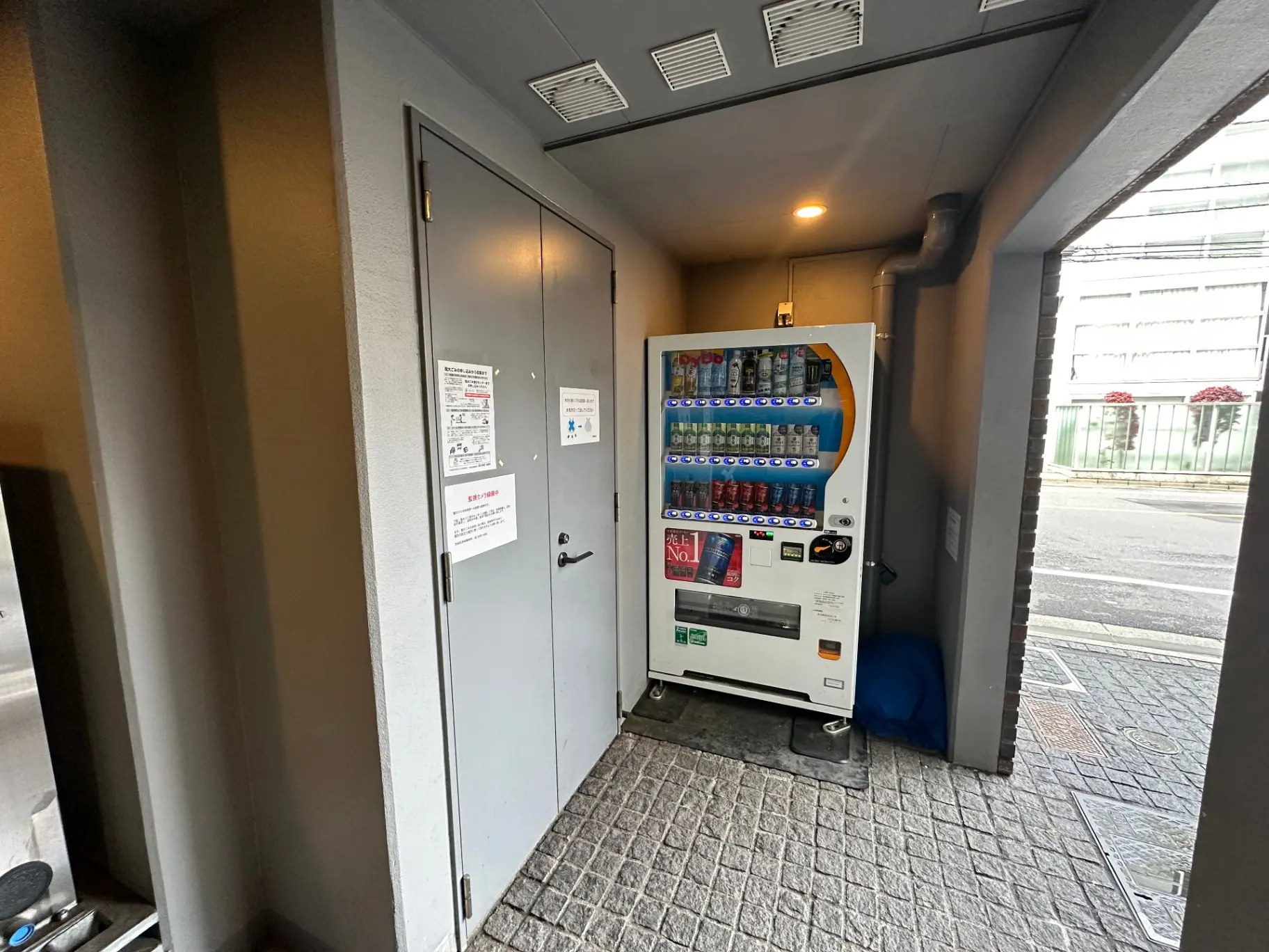 屋外に設置された飲料自動販売機、コンクリートの床と壁、通りから見える位置にある環境