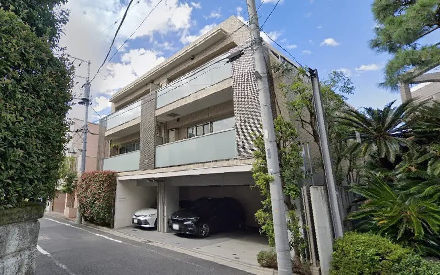 都会的な住宅街にあるモダンなデザインのマンション、車が停まっているガレージと周囲の緑が豊かな風景