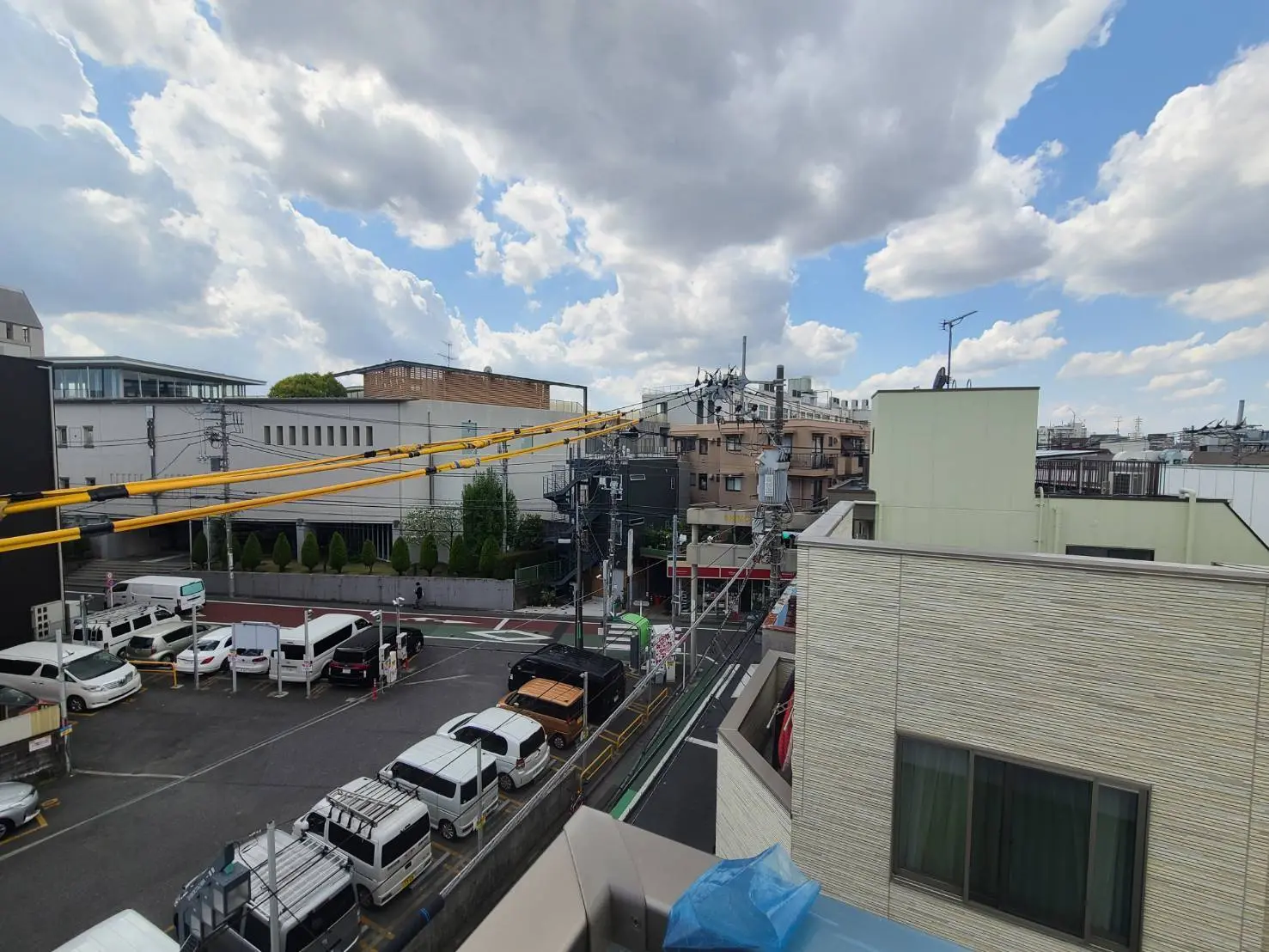 都会の風景、ビルと住宅が混在する街並み、晴れた空と雲、駐車場と道路の様子