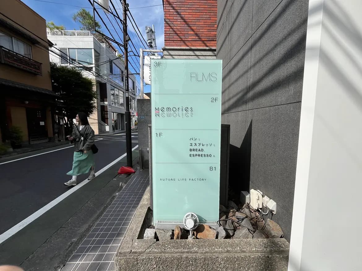 - 透明な看板に記載された飲食店の案内、1階はパンとエスプレッソ、2階はFILMS、3階はメモリーズの店舗名が表示された街の風景