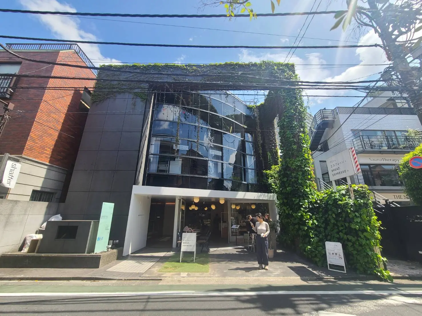 モダンで緑豊かな外観のビル、サウナとカフェの看板が見える、都会のオフィス街の景観