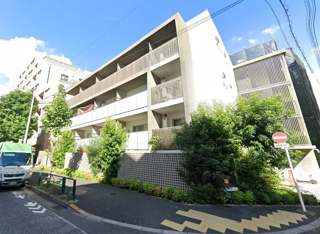 日本の都市部にあるモダンなマンションの外観、緑豊かな植栽、晴れた日の青空