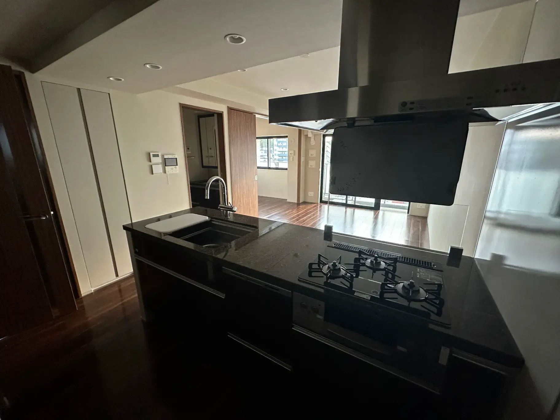 モダンなキッチン、ダークブラウンのキャビネットとガスレンジ、レンジフード、光が差し込む明るい部屋