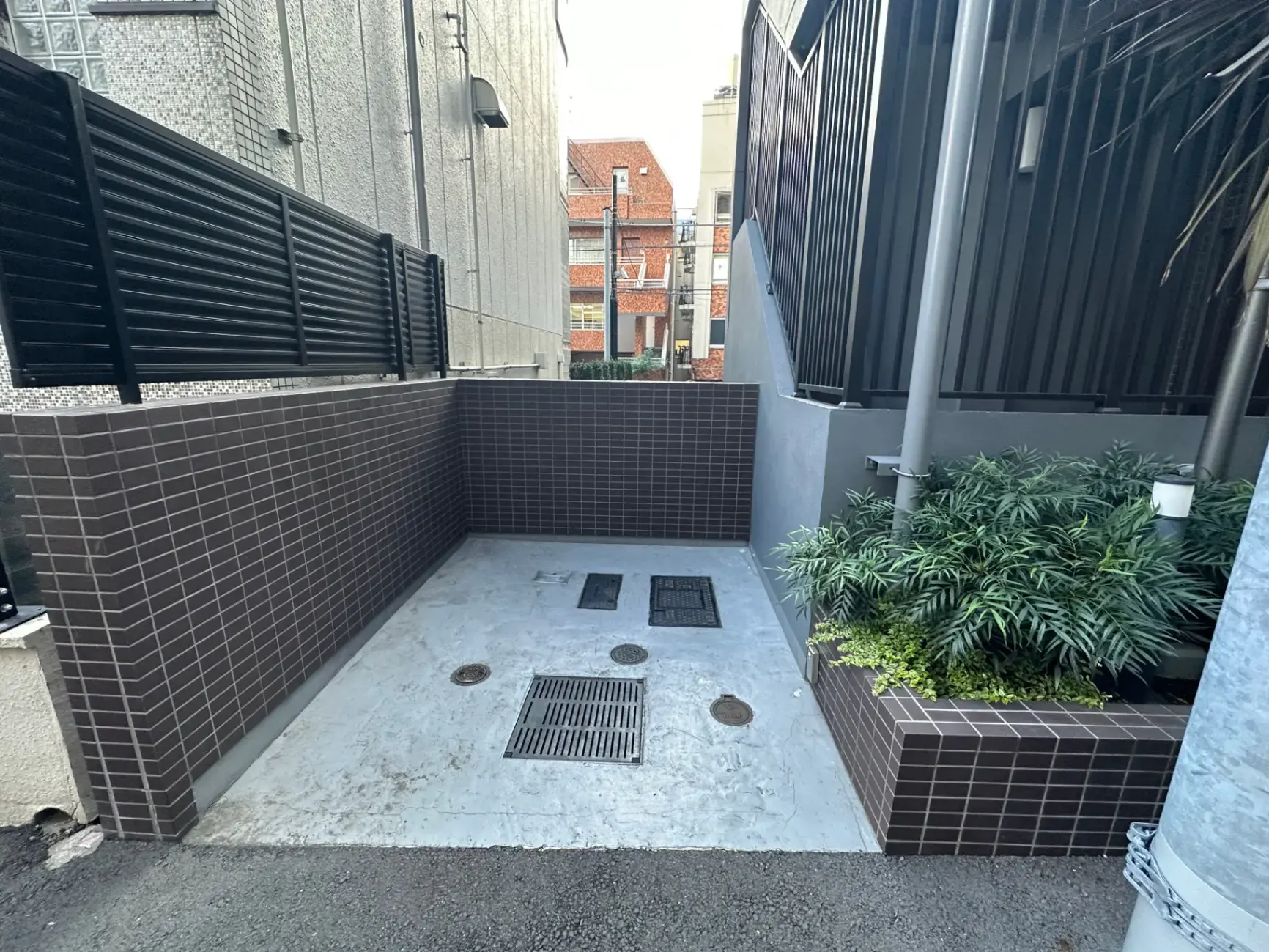 都市のビル間の狭いスペースに設計されたモダンな庭園、茶色のタイルと緑植物が特徴