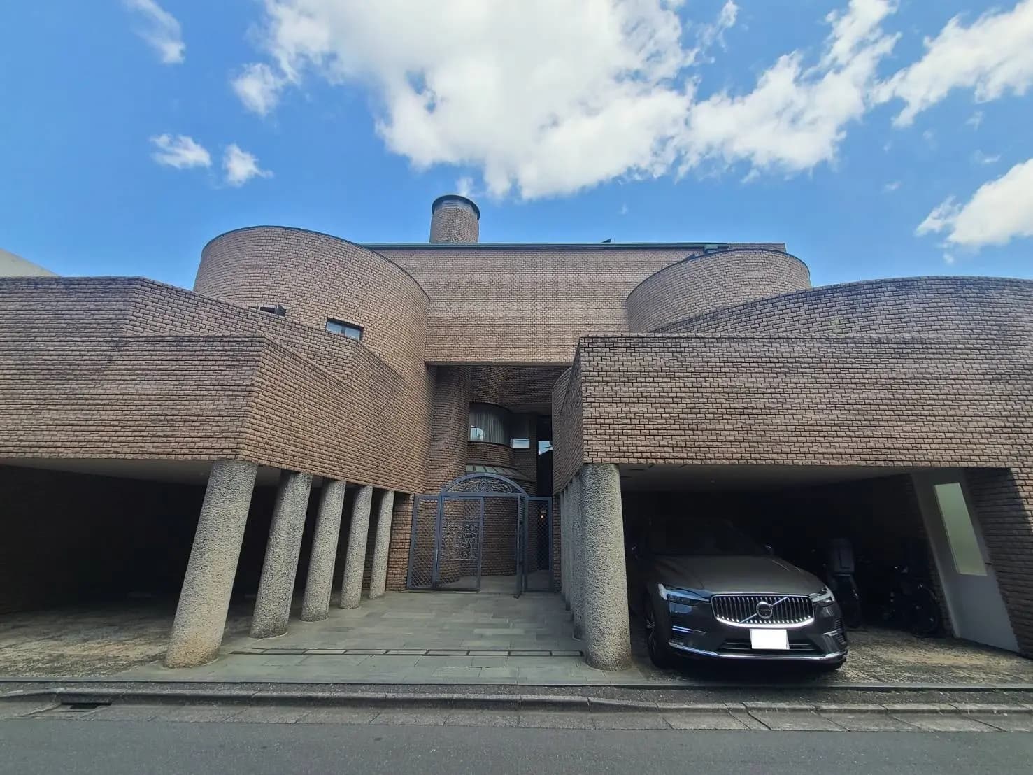 独特なデザインのモダン建築住宅、円形のフォルムとレンガ造り、車が停まるガレージ付き