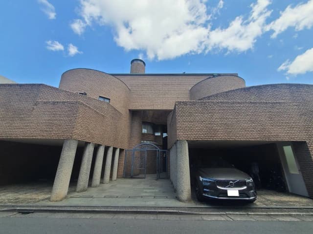 独特なデザインのモダン建築住宅、円形のフォルムとレンガ造り、車が停まるガレージ付き