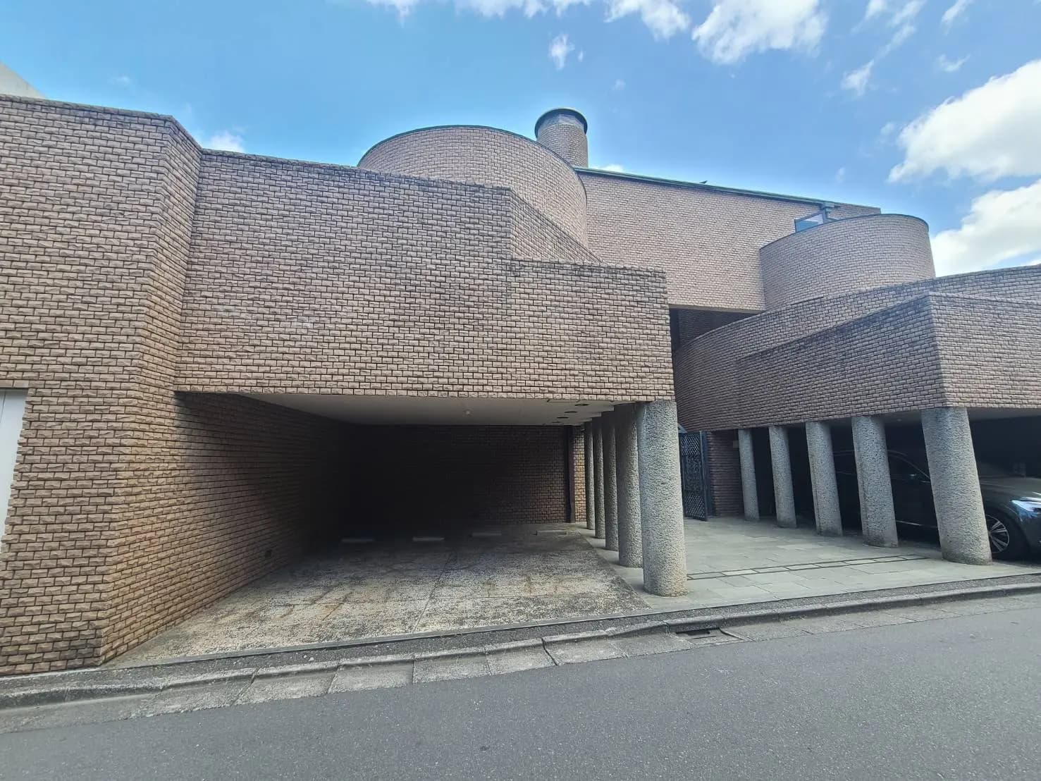 現代的な建築デザインの外観、特徴的なレンガ壁と円形の形状、青空と自然光が映える景観
