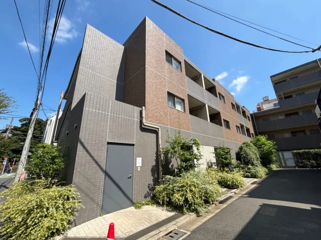 - モダンな外観のアパートメントビル、グレーと茶色のタイル張り、青空と緑豊かな植栽がある風景