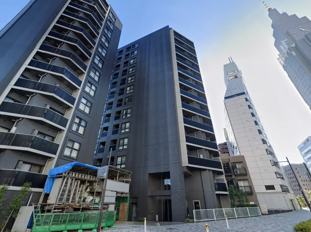 - 現代的なデザインの高層マンション、外観にはバルコニーがあり、周囲には建設中の構造物と隣接したオフィスビルが立ち並ぶ景観