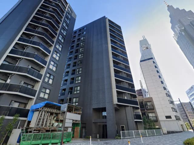 - 現代的なデザインの高層マンション、外観にはバルコニーがあり、周囲には建設中の構造物と隣接したオフィスビルが立ち並ぶ景観