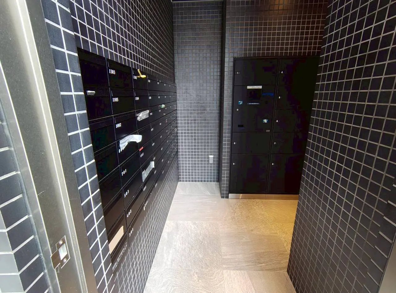 - シンプルでモダンなデザインの郵便ボックスと収納ロッカーのエリア、黒いタイルの壁と明るい床材の廊下