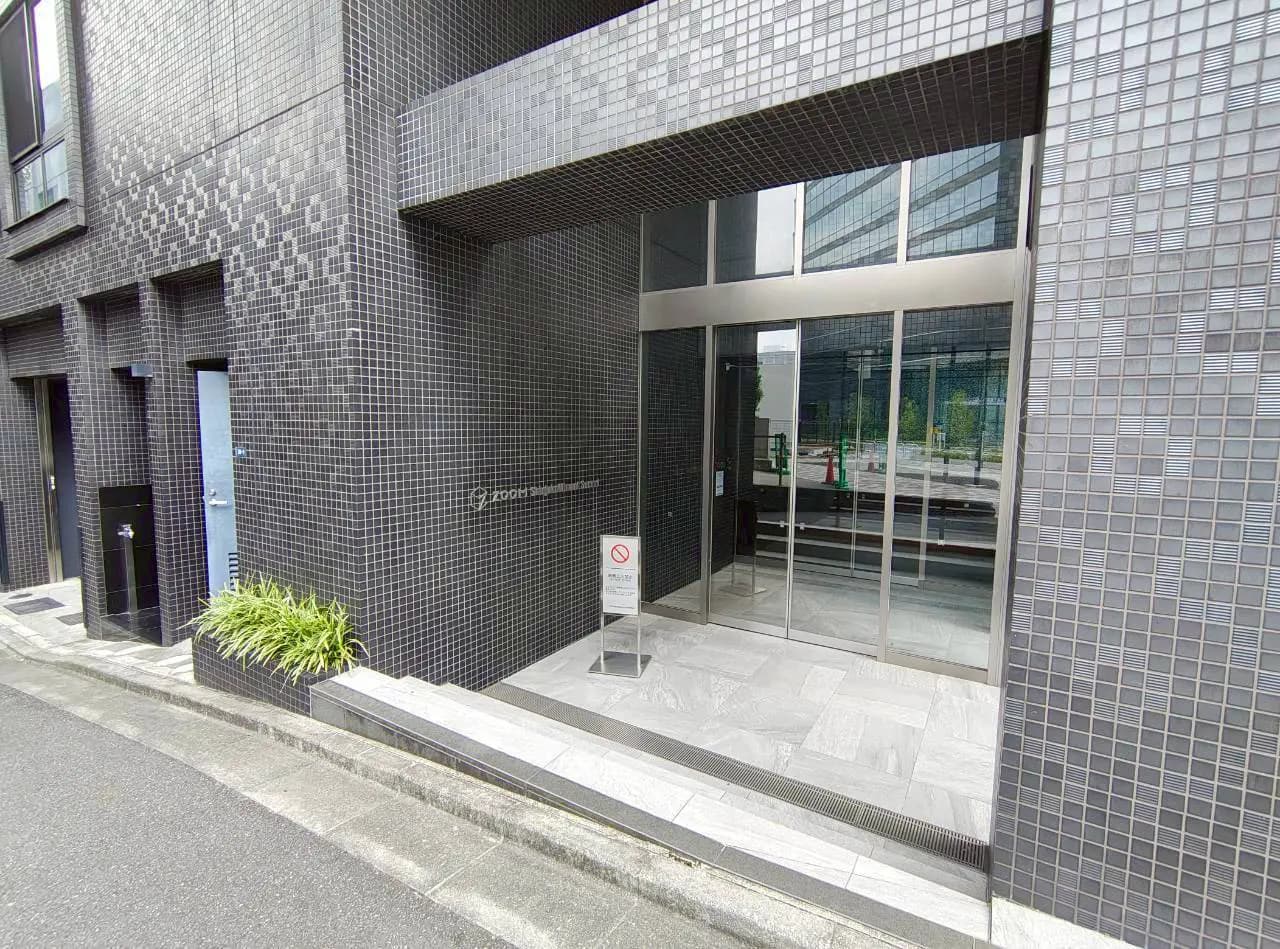 - 現代的な外観のビルのエントランス、黒いタイル張りの壁とガラスドア、周囲には緑の植栽が施されたデザイン