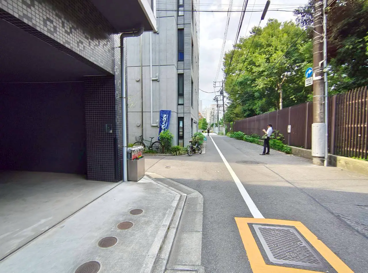 - 駐車場の出口近くにある都市の風景、左に自転車と植栽、右に立つビジネスマンと近くのビルが映る街角の写真
