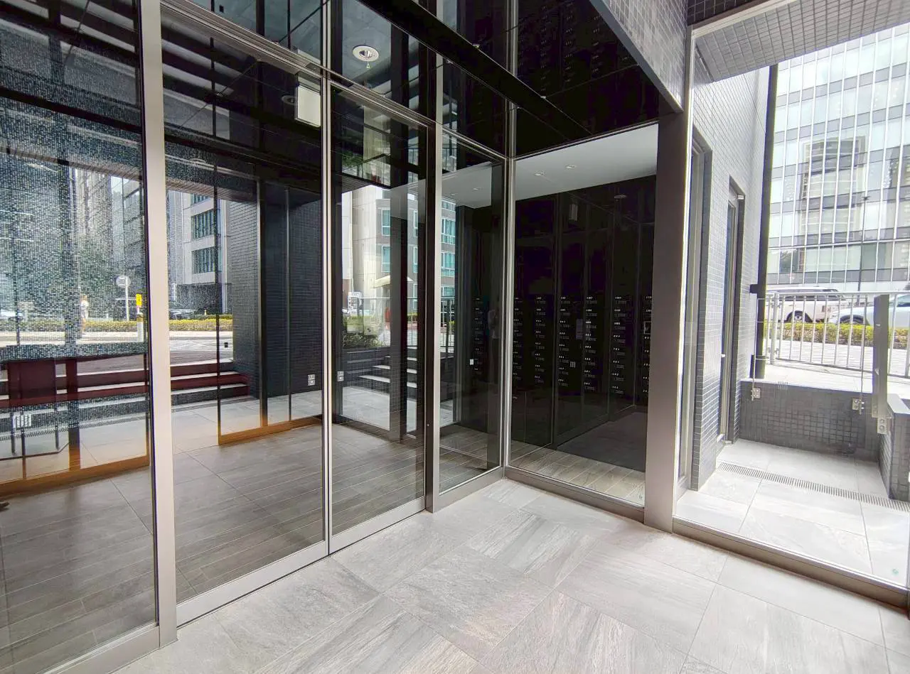 - 近代的なデザインのエントランス、ガラス扉と明るい床材、外部の景色が見える開放感のある空間