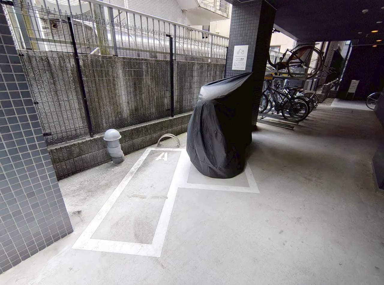- 自転車置き場の一角、黒いカバーがかけられた自転車、固定されたバイクスタンドと周囲の壁の様子