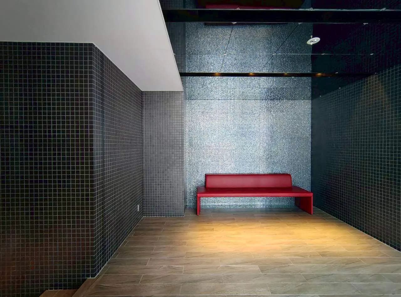 - シンプルなデザインの室内、黒いタイルの壁と赤いベンチが特長のモダンな空間、明るい床が印象的なインテリア