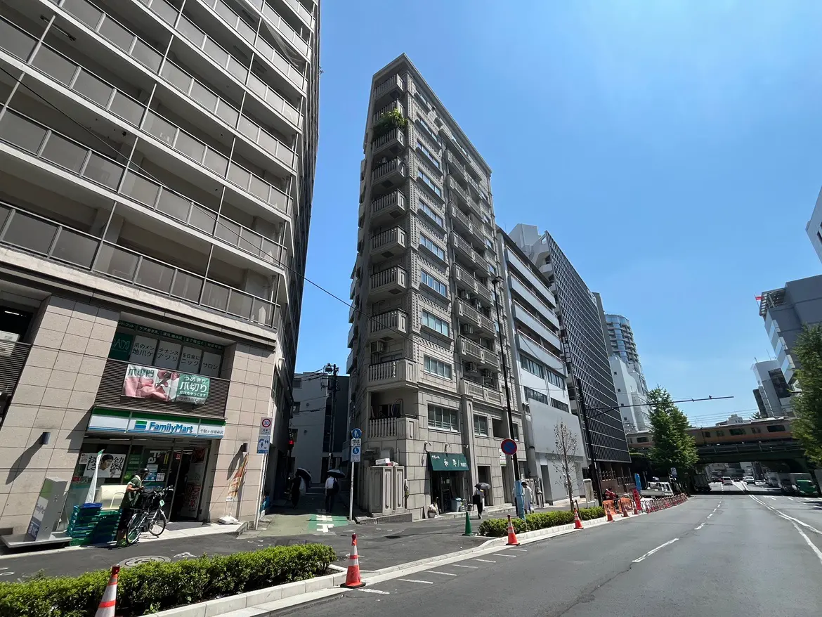 - 都会のビジネス街の風景、複数の高層ビルとコンビニエンスストアの店舗、青空の下で人々が行き交う様子