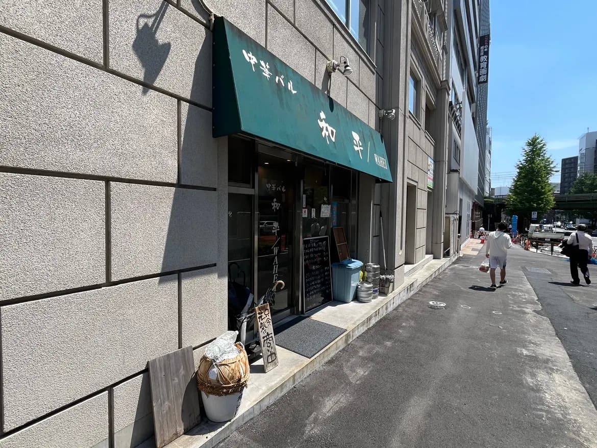 - 中華バル「和平」の外観、緑の看板と店頭の装飾、日差しが照らす街並みの風景