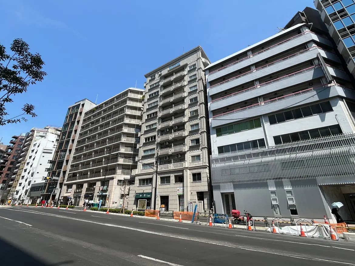 - 青空の下に立ち並ぶ高層ビル群、手前には工事中の道路と歩行者が見える都市の風景